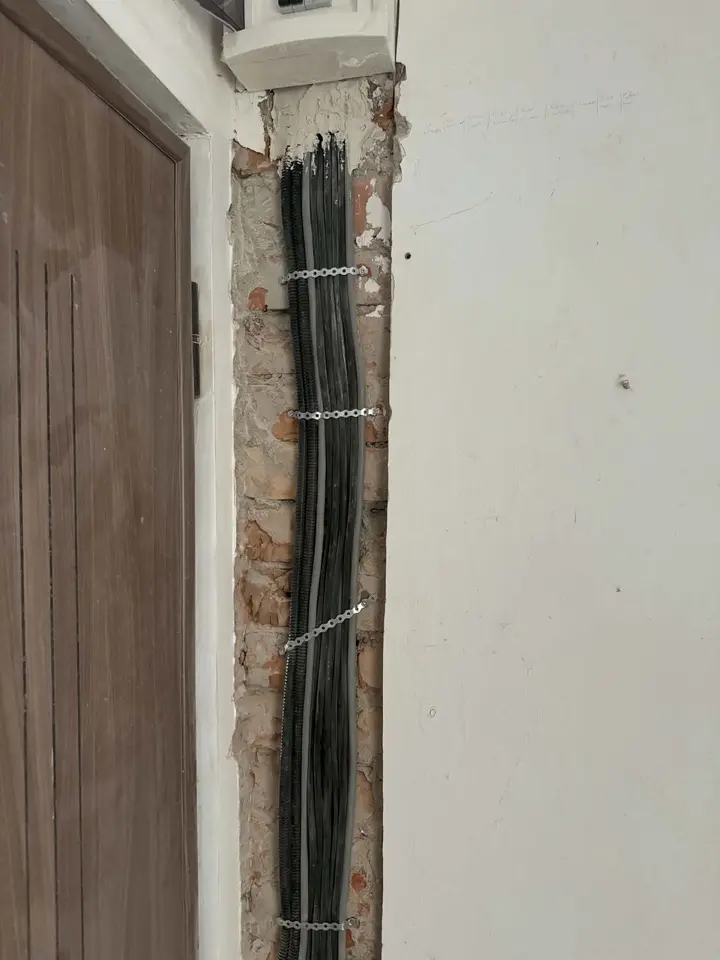 Mănunchi de cabluri fixate cu bride într-o ștrobă verticală, sub un tablou electric, lângă o ușă
