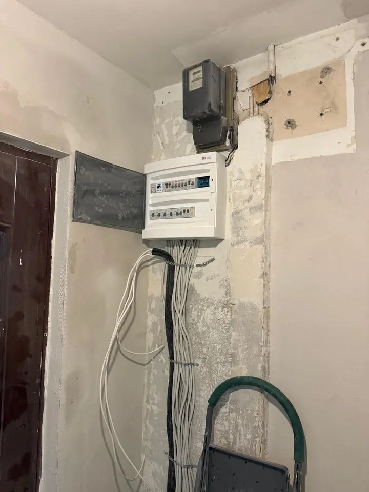 Tablou electric montat lângă contor, într-un hol în renovare, cu cabluri albe legate în mănunchi