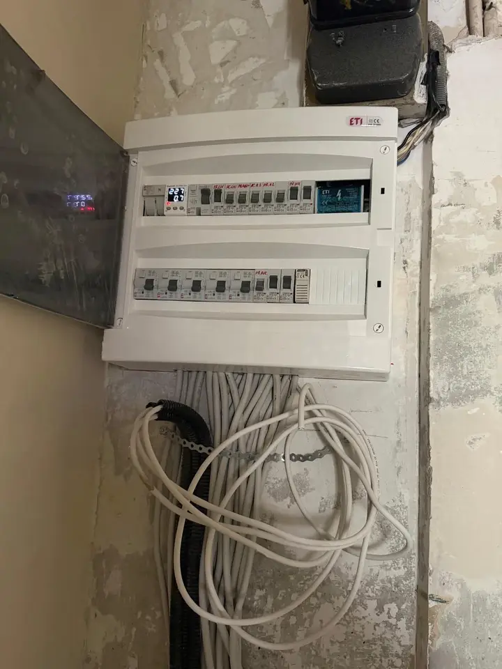 Tablou electric montat lângă contor, cu cabluri albe adunate într-un colac și tub gofrat negru