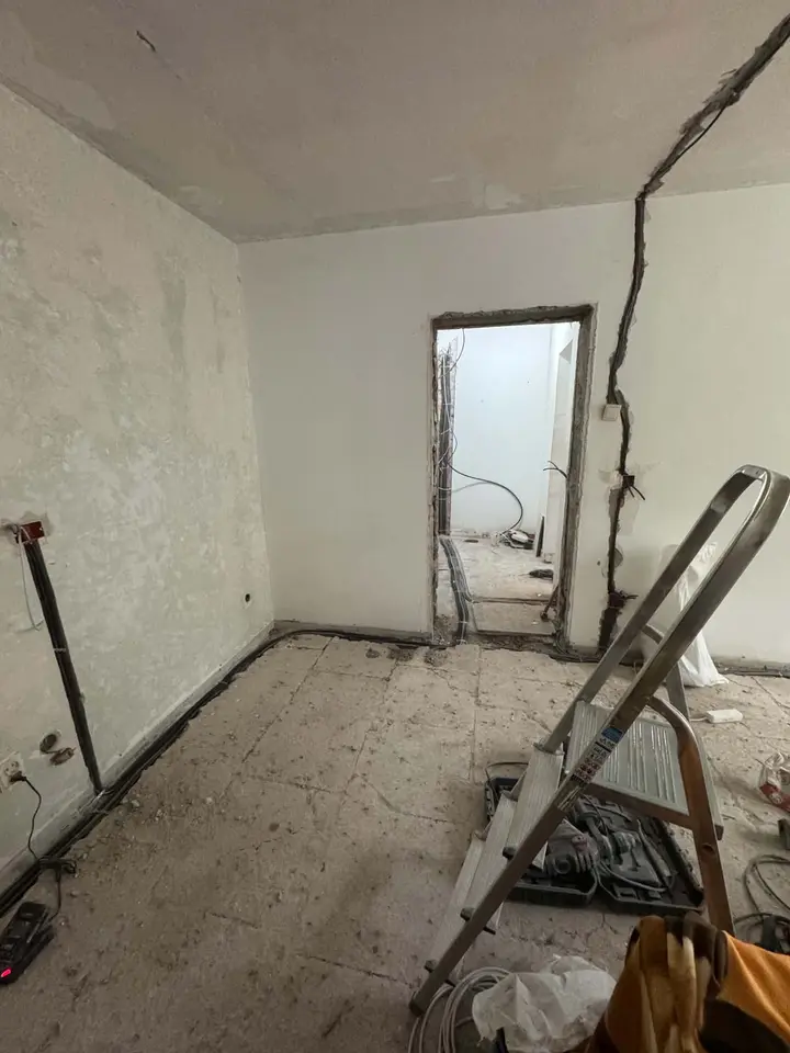 Cameră în renovare, cu trasee de cablu în perete și pe pardoseală și o ușă către holul cu tuburi pe jos